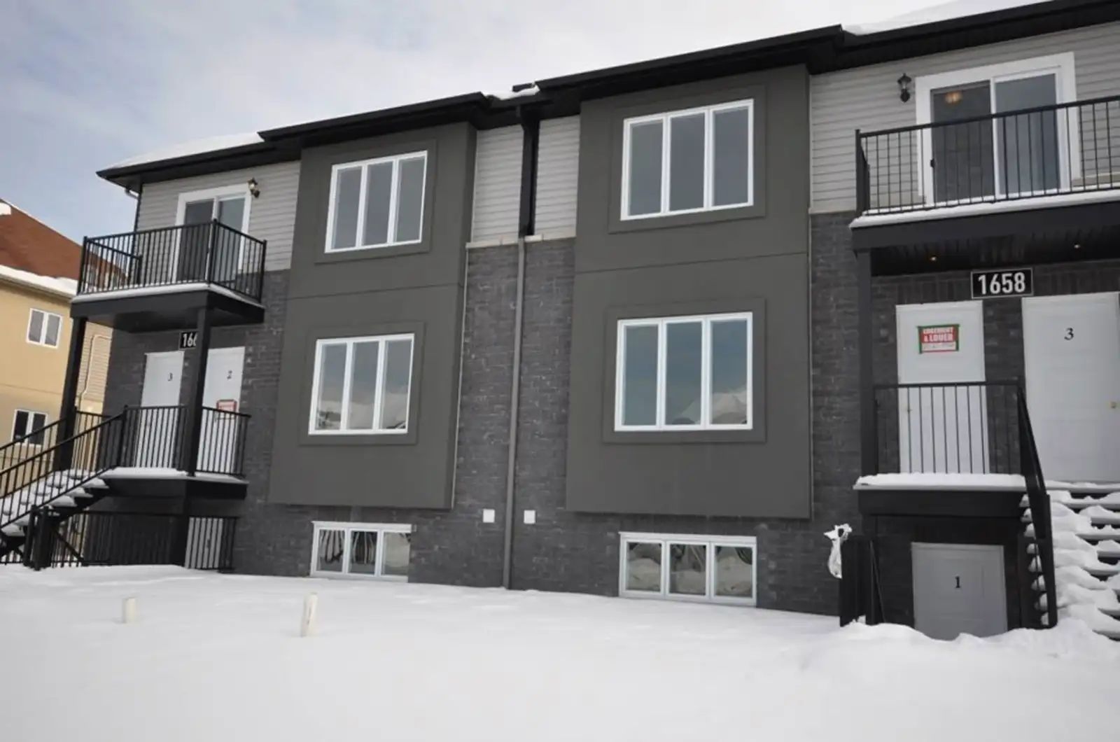 Immeuble à logements neuf bâti par Maisons Allaire : revêtement gris, soubassement de brique foncée, balcons et escaliers d'acier noir, portes numérotées, neige au sol